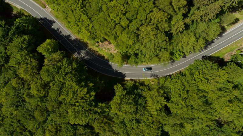 Vista aérea: Un coche circulando por una carretera a través de un bosque.