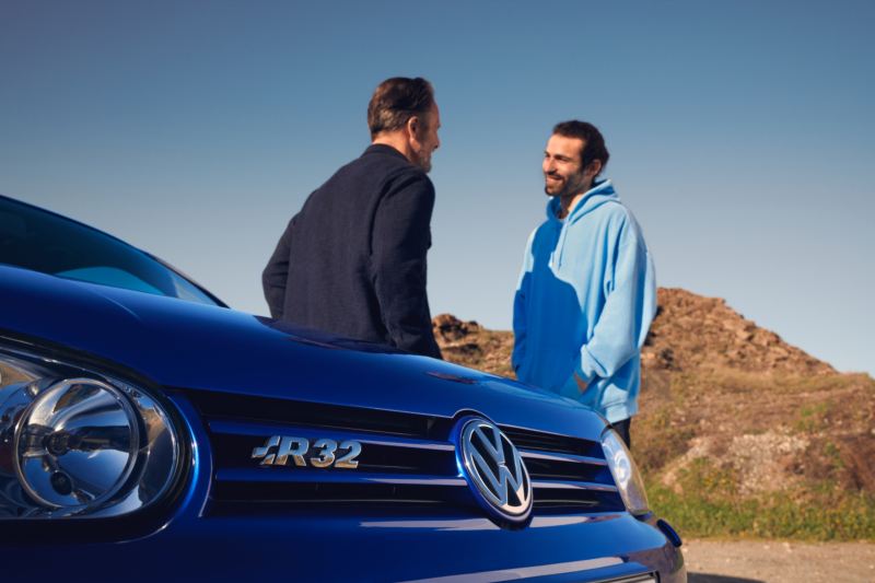 Dos chicos hablando junto a un Volkswagen Golf R con el detalle al emblema R32