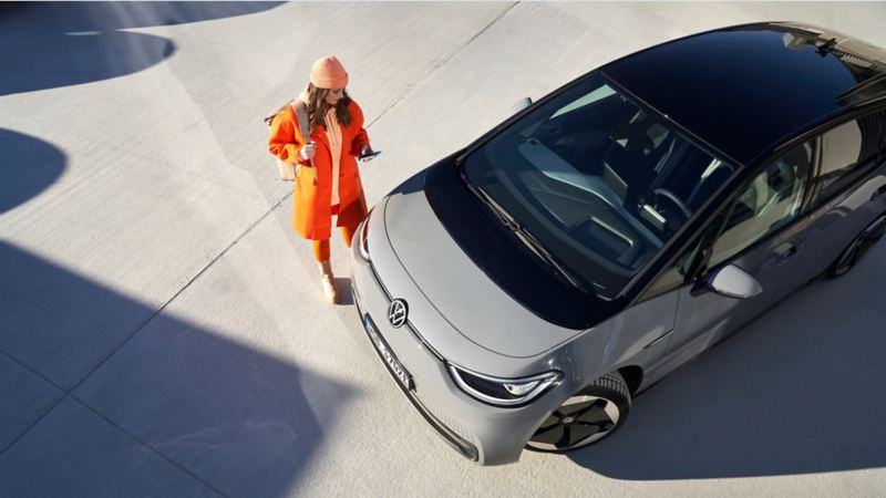 Chica de pie delante de un Volkswagen ID.3 de color gris.