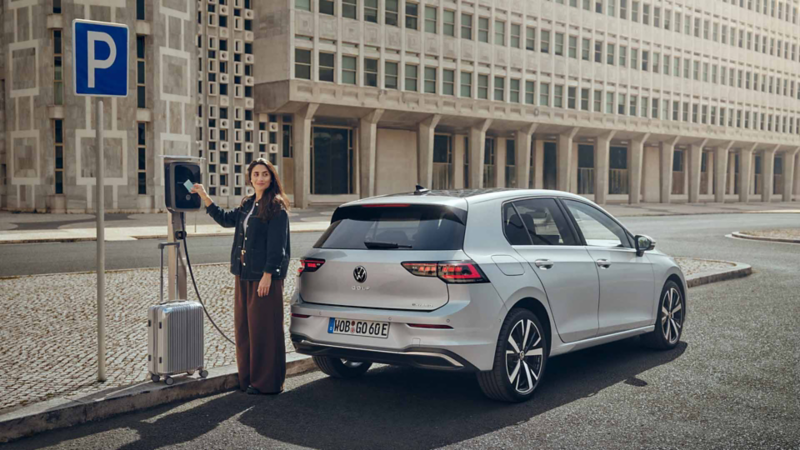 Una persona enchufando su Volkswagen en una estación de carga citadina
