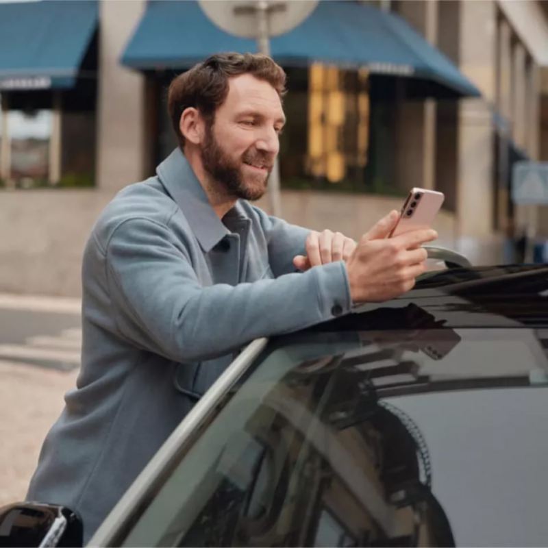 Un hombre con un smartphone apoyado sobre un Volkswagen