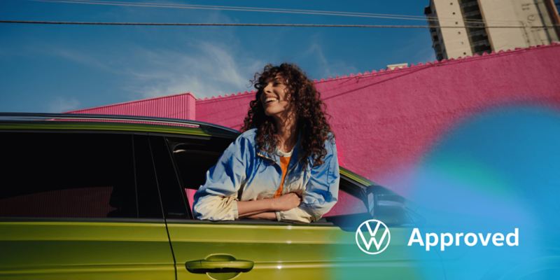 Una chica sonriendo en la ventanilla de un Taigo verde con el logo de Volkswagen Apporved