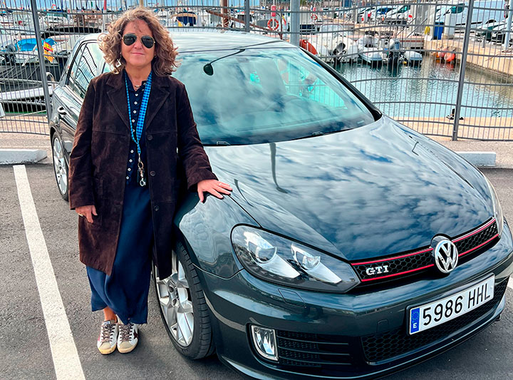 Una mujer apoyada en un Golf Volkswagen oscuro en un puerto