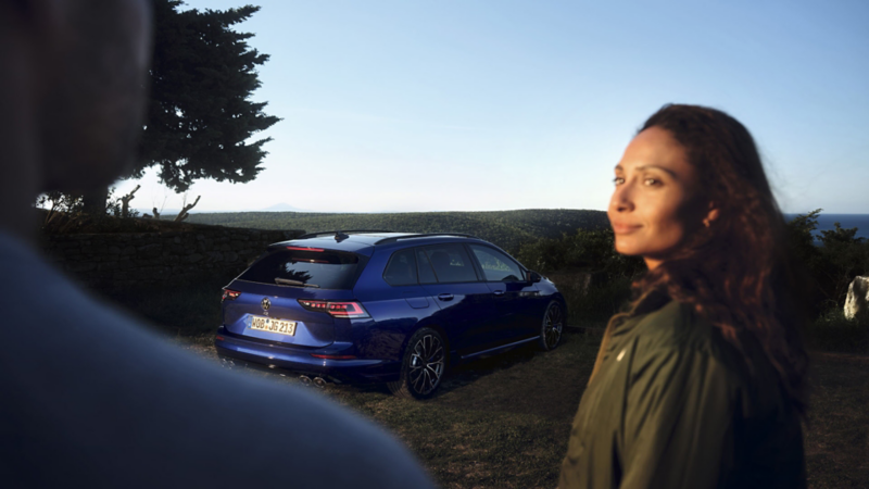 Un Volkswagen Golf Variant R azul aparcado en el campo con una mujer en primer plano