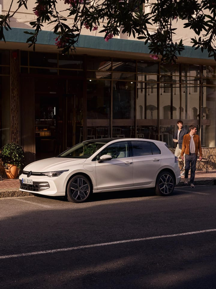 Dos chicos al lado de un Volkswagen de color blanco estacionado fuera de un establecimiento