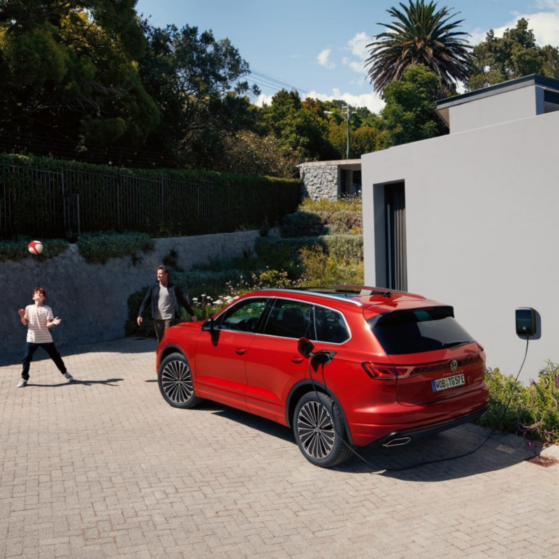 Un Volkswagen de color rojo conectado a carga estacionado al lado de una casa