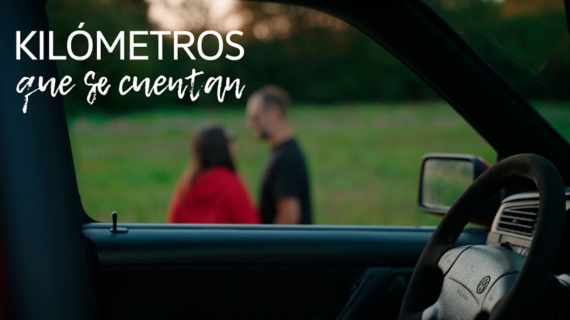 Detalle del interior de un Golf GTI 20 Aniversario con las ventanillas bajadas, al fondo Rodrigo y su pareja sobre un campo verde