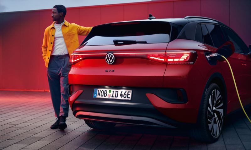 Un chico apoyado en un Volkswagen ID.4 GTX rojo visto desde atrás y conectado a un cargador
