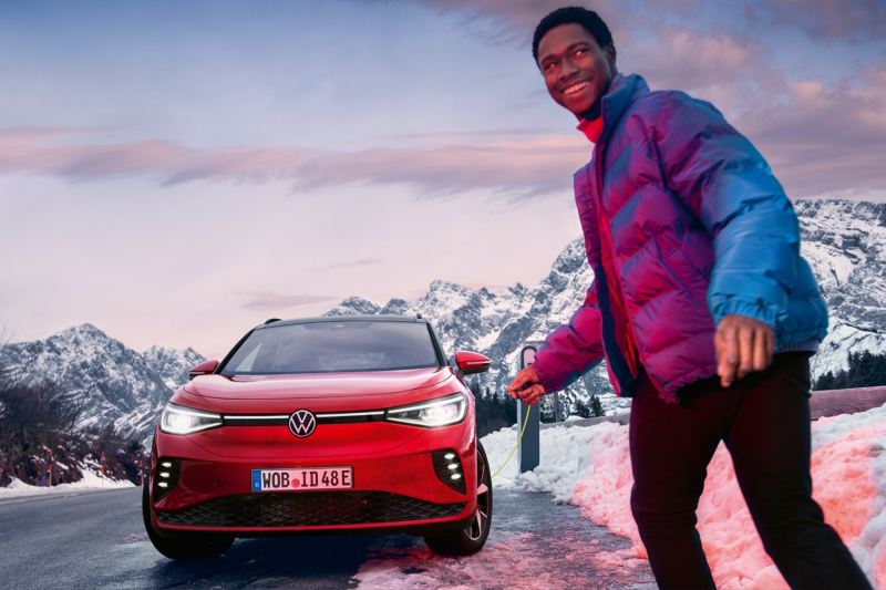 Un hombre junto a un Volkswagen ID.4 GTX conectado a un cargador en una carretera de montaña nevada