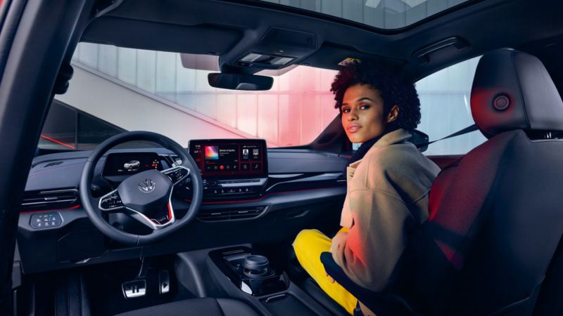 Chica sentada en el puesto de copiloto de un Volkswagen ID.4 GTX y vista del salpicadero