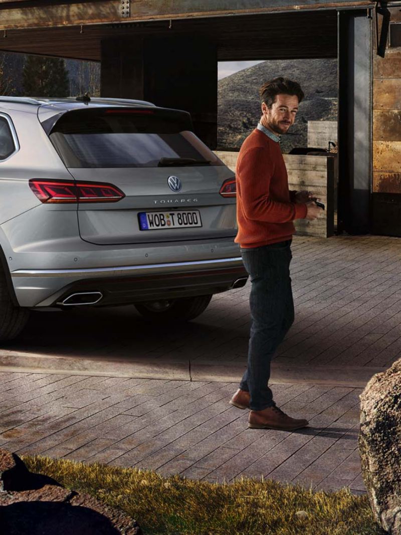Un hombre de pie delante de un Volkswagen Touareg aparcado en casa