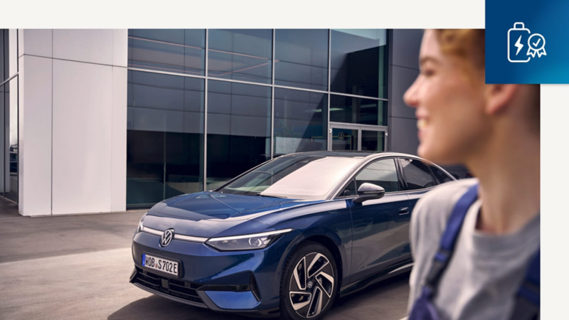 Exterior de un concesionario Volkswagen con una trabajadora y un Volkswagen Approved detrás