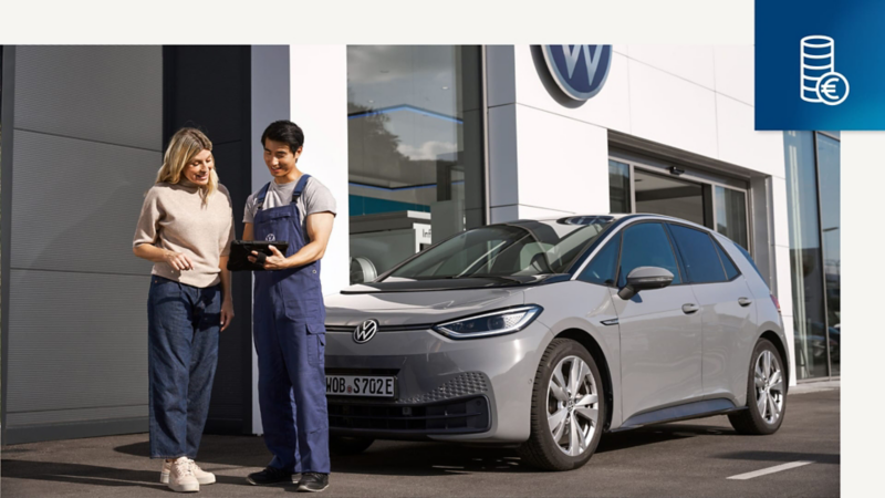 Un trabajador de Volkswagen delante de un Volkswagen Approved mostrandole resultados de la revisión a otra persona