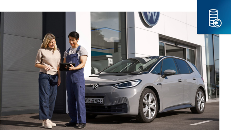 Un trabajador de Volkswagen delante de un Volkswagen Approved mostrandole resultados de la revisión a otra persona