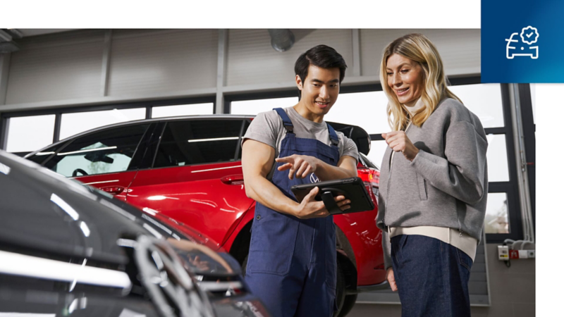 Un trabajador de Volkswagen con una tablet en la mano mostrándole mejoras a su dueña dentro de un concesionario Volkswagen