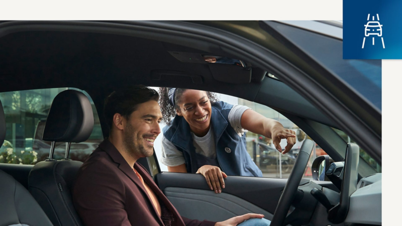 Detalle del interior de un Volkswagen Approved, una persona en el asiento delantero y otra desde fuera ayudandole