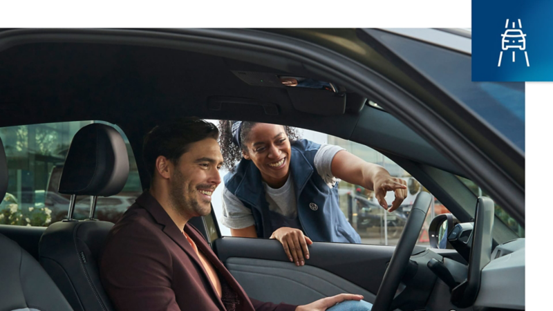 Detalle del interior de un Volkswagen Approved, una persona en el asiento delantero y otra desde fuera ayudandole