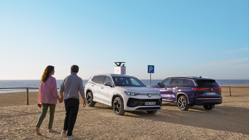 Una pareja al lado de dos Volkswagen híbridos estacionado en la playa