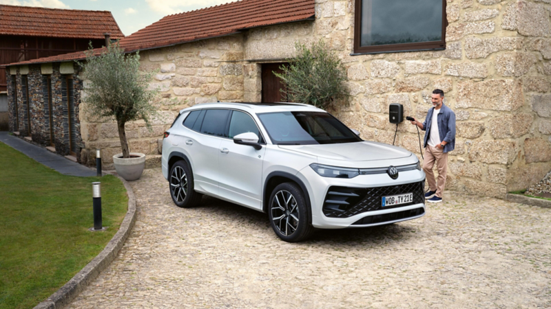 Un hombre cargando un Volkswagen híbrido junto una casa