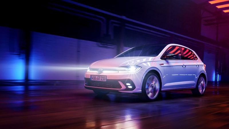 Un Volkswagen Polo GTI blanco circulando de noche iluminado por luces azules y rojas