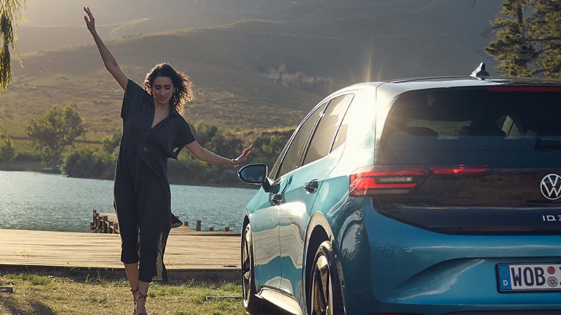 Una mujer con las manos en alto junto un Volkswagen ID.4 GTX azul