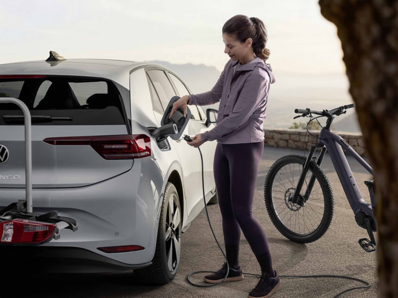 Una mujer cargando un Volkswagen plateado vestida de deporto junto a una bicicleta