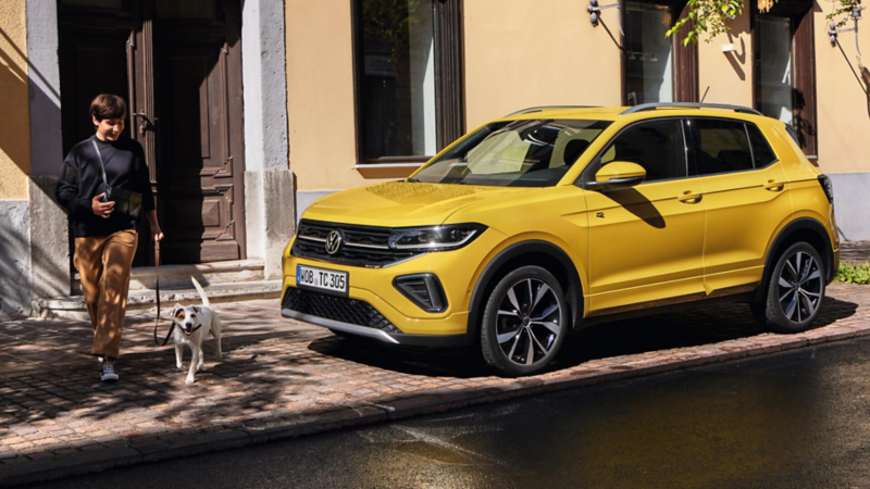 chico junto a su perro al lado de un Volkswagen T-Cross amarillo estacionado fuera de una casa