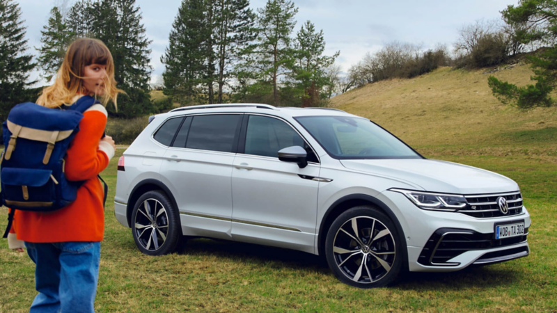 chica junto a un Volkswagen Tiguan Allspace blanco estacionado en el campo