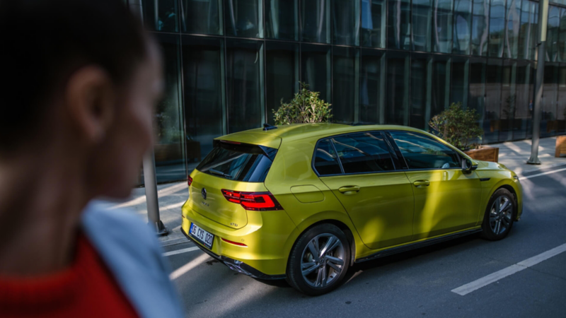 Un chico mirando un Volkswagen Golf de color verde claro estacionado en la calle