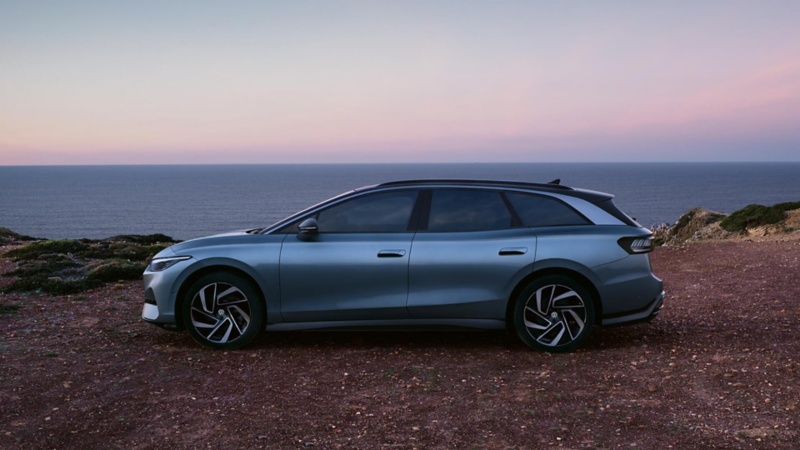 Un Volkswagen ID.7 Tourer de color azul metalizado estacionado al lado de un acantilado vista lateral