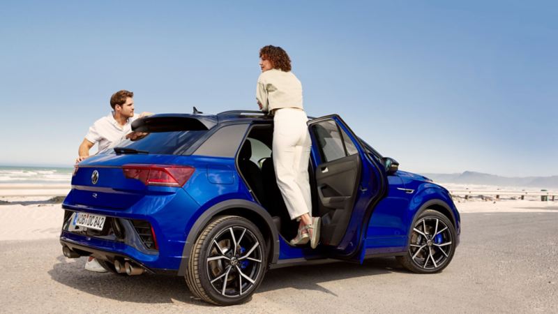Dos personas junto a un Volkswagen T-Roc R de color azul oscuro estacionado en la playa