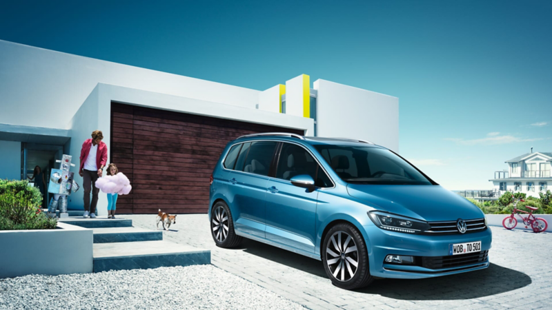 Una familia dirigiendose a un Volkswagen Touran azul aparcado delante del garage