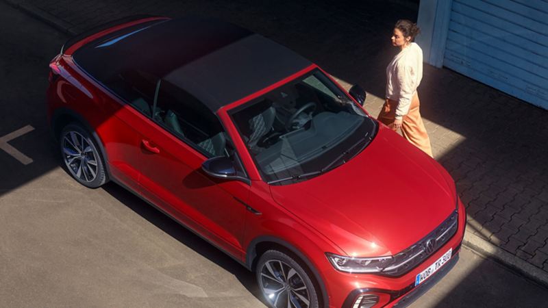 mujer abriendo la puerta de un Volkswagen T-Roc Cabrio rojo vista zenital lateral estacionado en la calle
