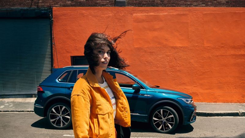 chica al lado de un Volkswagen Tiguan azul estacionado en la calle vista lateral