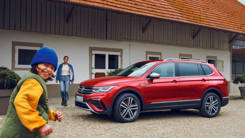 madre e hijo junto a Volkswagen Tiguan Allspace rojo estacionado delante de una casa