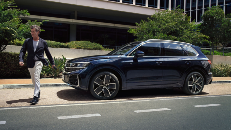 hombre junto a un Volkswagen Touareg azul estacionado en la calle