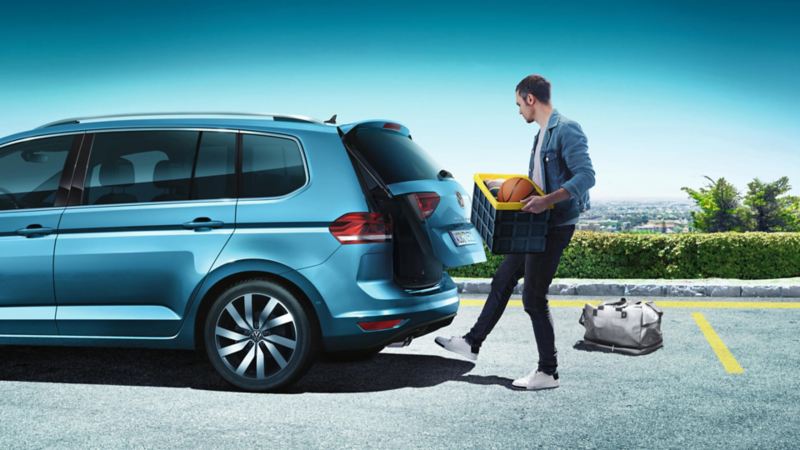 hombre abriendo el maletero de un Volkswagen Touran azul estacionado en la calle