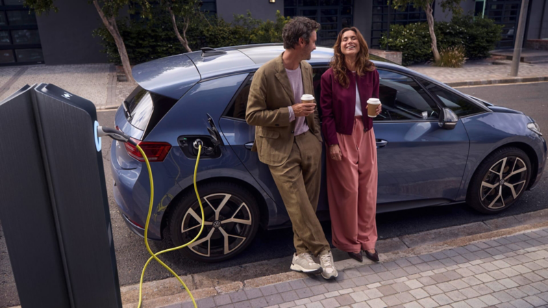 Una pareja apoyada sonriendo en un Volkswagen ID.3 Neo de color azul