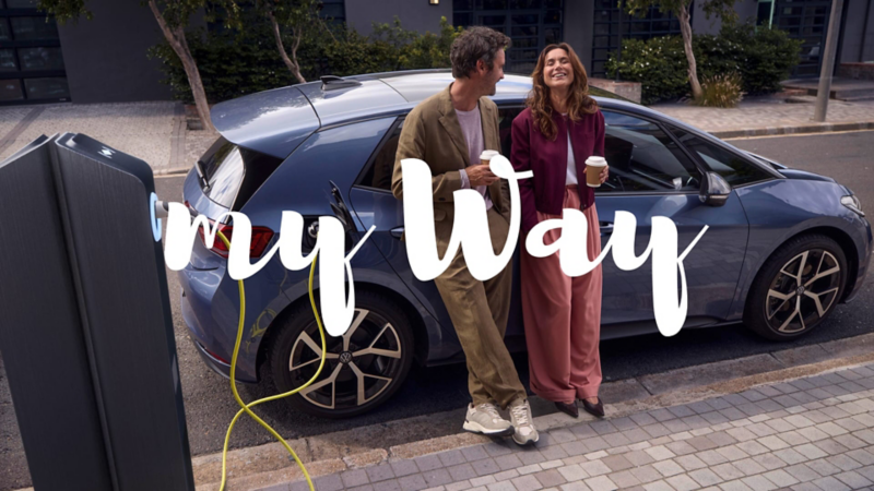 Una pareja apoyada sonriendo en un Volkswagen ID.3 Neo de color azul con el logo My Way