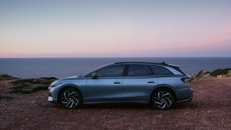 Un Volkswagen Id.7 tourer de color gris estacionado al lado de un acantilado con vistas al mar
