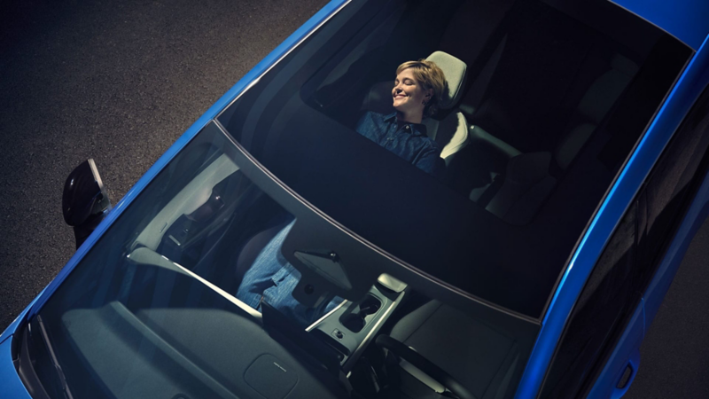 Vista desde arriba de Volkswagen ID.Polo con el techo abierto y una chica tumbada sonriendo en el interior
