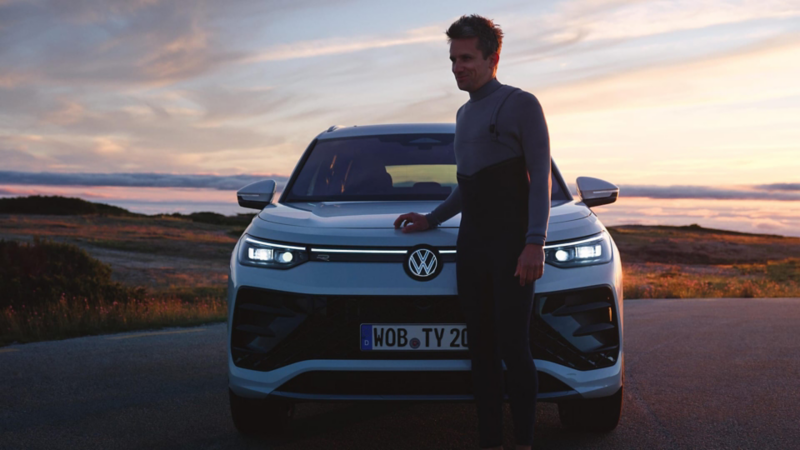 Un chico con traje de neopreno delante de un Volkswagen Tayron de color blanco