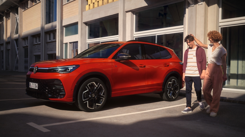 Una madre y un hijo al lado de un Tiguan de color rojo estacionado en una plaza de estacionamiento