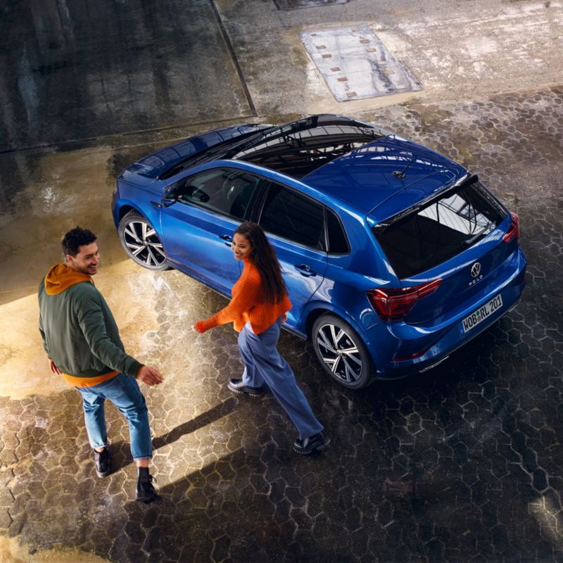 Una pareja junto a un Volkswagen Polo azul visto desde arriba