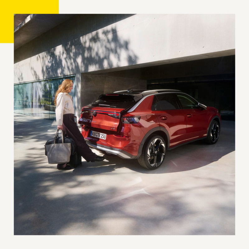 Un Nuevo T-Roc rojo aparcado en un espacio citadino y una persona cargando su maletero