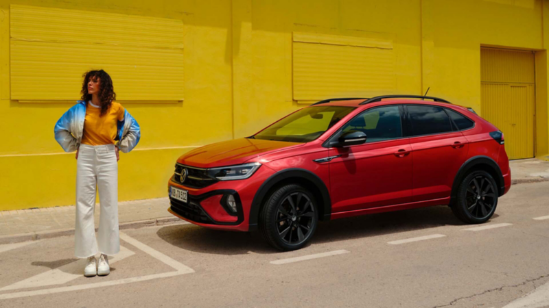 Una chica junto un Volkswagen Taigo rojo parado junto una pared amarilla