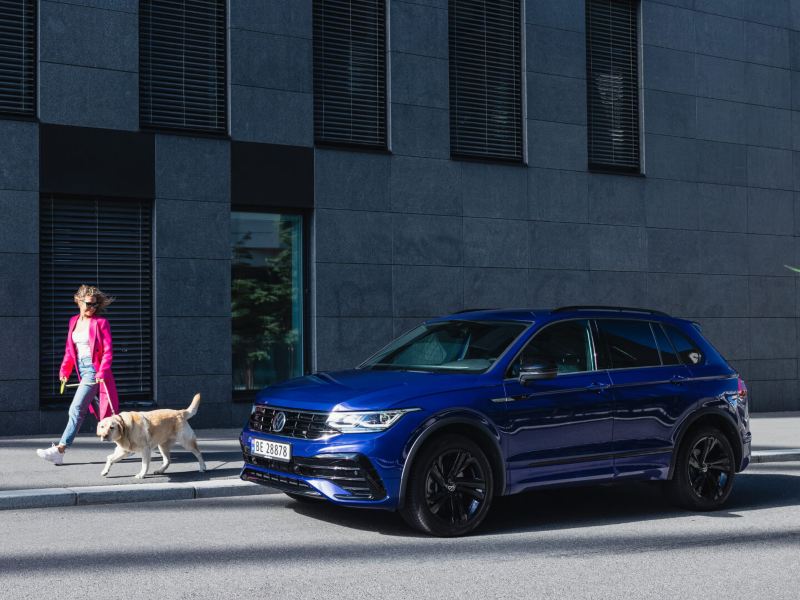 Mujer paseando con su perro al lado de un Volkswagen Tiguan azul