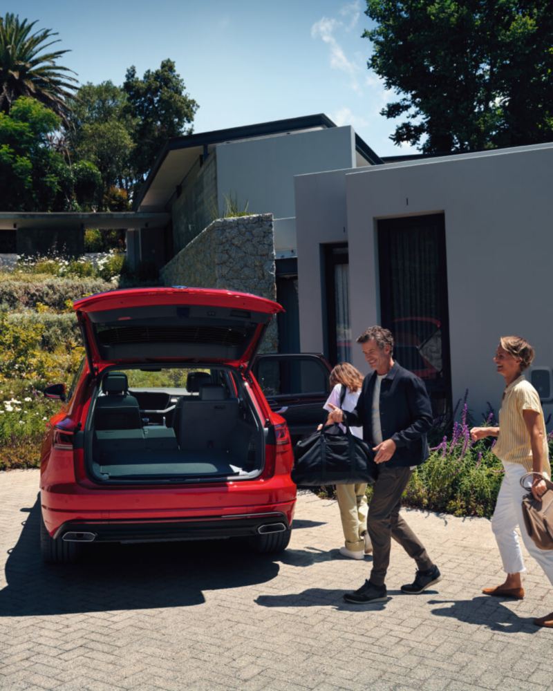 Una familia junto a un Volkswagen Touareg híbrido enchufable rojo aparcado en casa