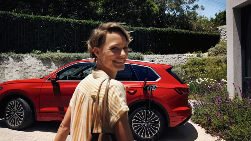 Chica sonriendo delante de un Volkswagen Touareg conectado a la carga en casa