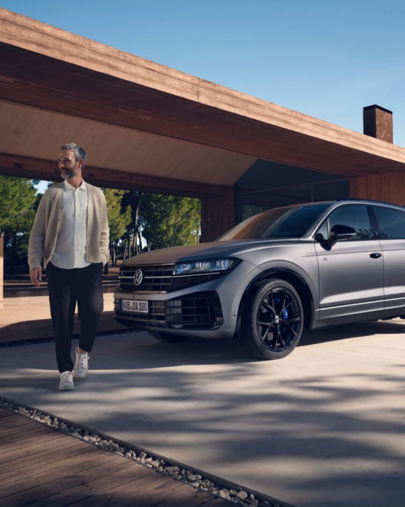 Un hombre junto a un Volkswagen Touareg híbrido enchufable gris aparcado en casa